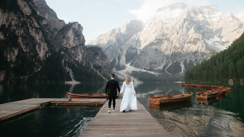 Novios caminando por un muelle frente a un lago y montañas en Italia