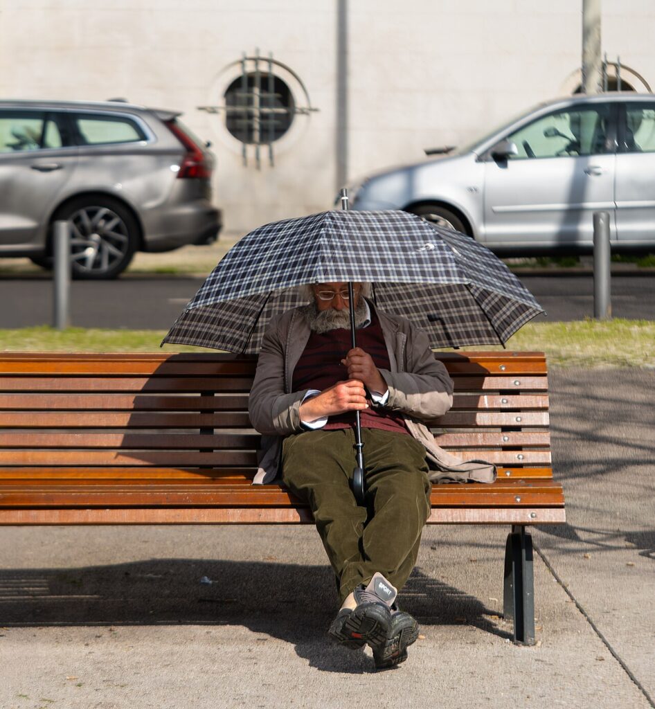 Adulto mayor dormido en una banca de un parque, bajo la sombra de una sombrilla
